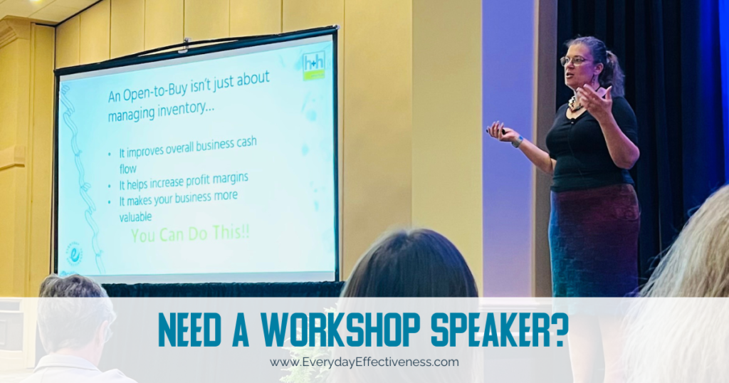 blog feature image shows Gwen on a stage addressing a crowd attending her Open to Buy workshop at h+h americas in 2023. She's wearing her blonde hair back in a ponytail and gesturing wildly. She's wearing a black scoop-neck blouse and hand-knitted skirt (of course she is)